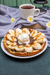 Obraz na płótnie Canvas Waffles with sliced banana, caramel sauce and whipping cream with a cup of tea