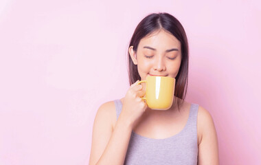 Healthy woman smile and drink morning coffee from yellow ceramic mug in morning breakfast,young asian girl isolated portrait pink color background ,copy space