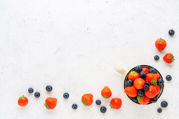 Fresh organic blueberry and strawberry in enameled mug on vintage white stone table.