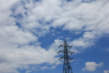 High-voltage electricity pole on clouds and blue sky background.