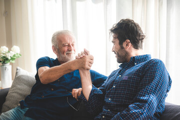 An adult hipster son and senior father relaxing and talking at home, stay and work from home for...