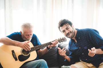 happy adult son and senior father playing guitar on sofa at home relaxing and having happy time with family