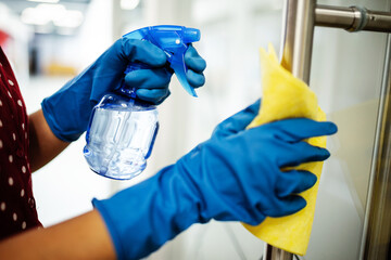 Closeup of woman's hands wearing blue rubber protective gloves spraying with sanitizer and cleaning...