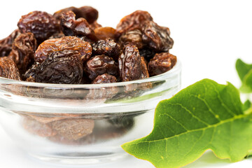 Raisins glass bowl with green leaf on white background.