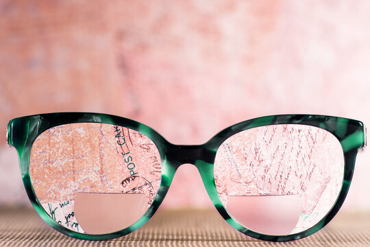 Eyeglasses Glasses with Bifocals and Black blue Frame smudged agaist written letters.  Blurry Vision Concept