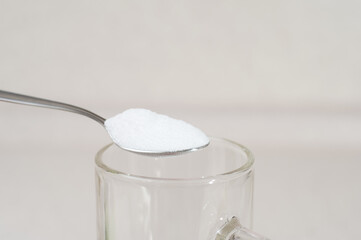 White tasteless creatine powder on a teaspoon over a transparent glass. Sports supplements and nutrition for recovery and progress