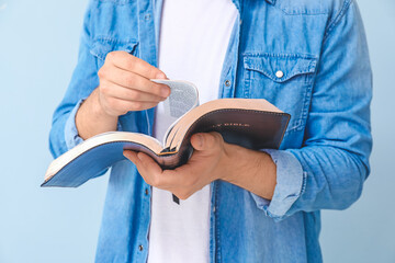 Young man reading Bible on color background, closeup