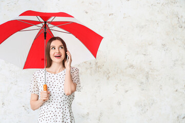 Beautiful woman with umbrella talking by mobile phone on light background