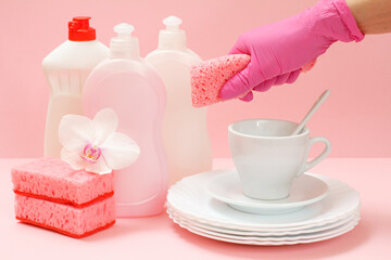 Woman's hand in protective glove with a sponge and utensil on a pink background.