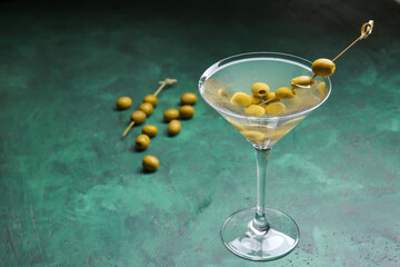 Glass of tasty martini cocktail with olives on color background