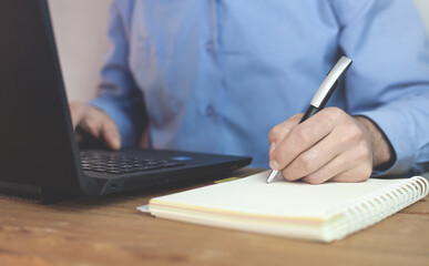 Man typing in keyboard and writing on notepad.