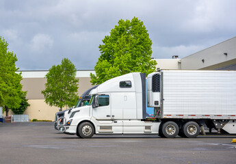 Big rig semi trucks with refrigerator semi trailer loading frozen cargo standing at warehouse dock...