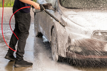 a man washes a brown car with a gun for washing high pressure cars