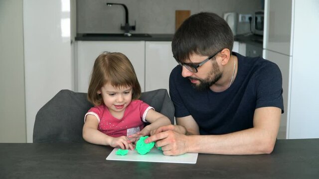 Portrait of happy child girl with young father learn to sculpt from green plasticine. Smiling 3 year old daughter with father spend time on children's creativity
