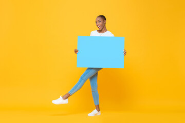 Fun full length portrait of smiling African American woman holding and showing blue placard in...