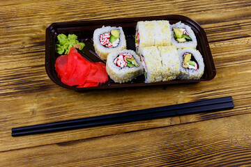 Uramaki sushi rolls with surimi in plastic box on wooden table. Top view. Sushi for take away or delivery of sushi in plastic container