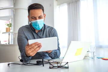 Fototapeta na wymiar Businessman looking at a tablet PC wearing a healthcare face mask. Man in a medical mask at the office. Businessman with mask using digital tablet at work
