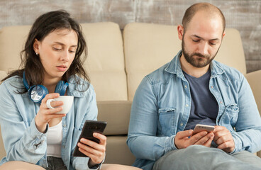 Couple checking social media on smartphones while relaxing on floor.