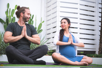 Young couple of beautiful pregnant woman and handsome husband practicing yoga and exercise in garden house.