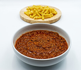 Traditional italian ragù (bolognese sauce) with raw pasta on the background. Selective focus