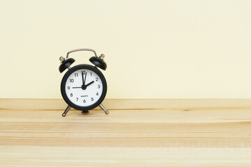 A small black alarm clock on a light yellow background with space for text.
