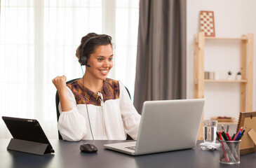 Excited female entrepreneur during a video call on laptop from home office.