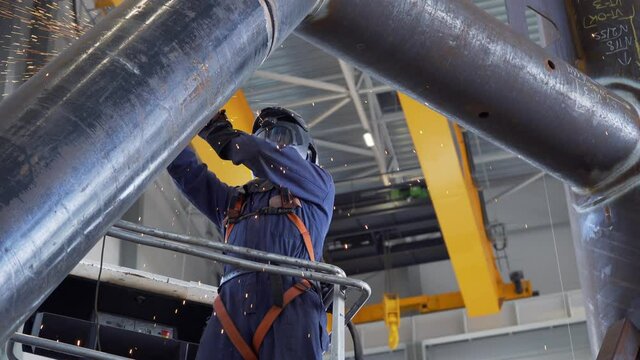 Professional heavy industry worker welder in protective mask and suit works with metal construction on factory. Steel and iron welding construction site. Welding machine with sparks and flashes.