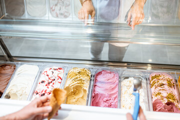 Salesman picking ice cream with a spoon from refrigerator in the store. View from above on a trays...