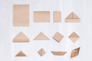 Steps of making origami paper boat on white wooden background.
