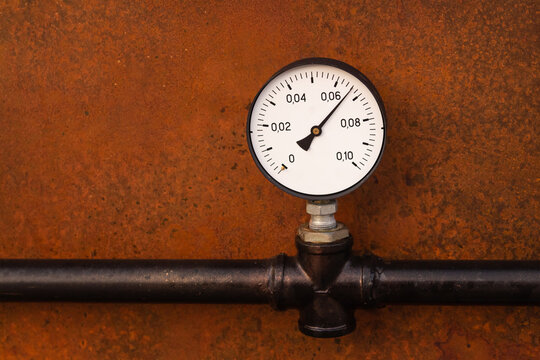 pressure gauge on a background of a rusty old iron wall and a black pipe