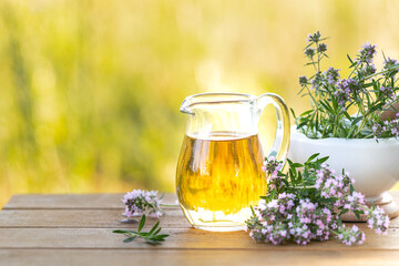 Thyme essential oil in a glass jug and branches of a fresh thyme plant with flowers on a wooden background. Copy space