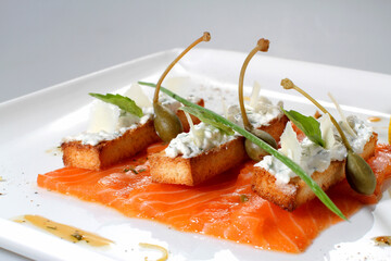 Croutons with salmon, white cheese and capers on a white plate