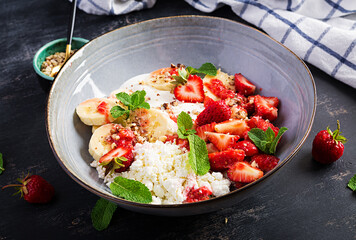 Cottage cheese or curd cheese with strawberries, bananas, walnuts in a blue bowl. Healthy food.