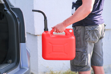 Red canister in the hands of a man. Filling a stalled car with gasoline from a canister.