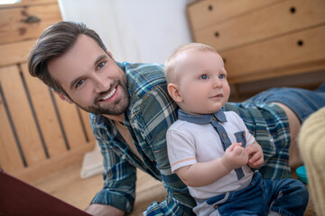 Dark-haired handsome father smiling laying to his son on the floor