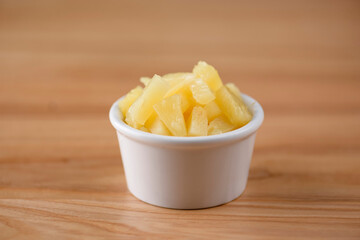 Pineapple chunks in the bowl isolated on wooden background. Snack, appetizer. Pizza ingredient.