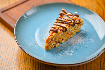 A piece of anthill cake with chocolate served on a blue plate over rustic wooden table. Sweet delicious dessert.