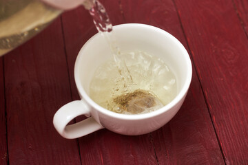 Tea bag in a white cup. Add boiling water to the cup. Making delicious herbal tea.