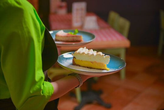 Waiter serves slice of lemon meringue pie in a blue plate. Delicious dessert. Eating out in restaurant.