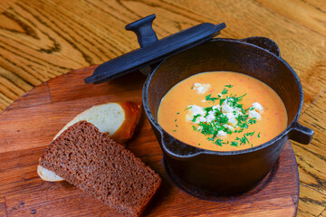 Pot with pumpkin soup with cheese and meat and pieces of bread served on wooden board over rustic...
