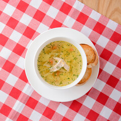 Chicken soup with vegetables and meat served in a white bowl over rustic wooden background with red...