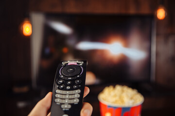 Craft bowl of popcorn on the dark table and TV remote control with TV set