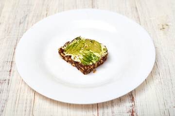 Slice of cereal bread with cream cheese and avocado on a white plate. Vegetarian sandwich.