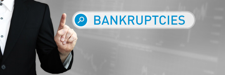 Bankruptcies. Businessman (Man) in a suit pointing with his finger to a search box. The word is in focus. Blue Background. Business, Finance, Statistics, Analysis, Economy