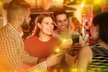 Young positive cheerful people with cocktails having fun at nightclub