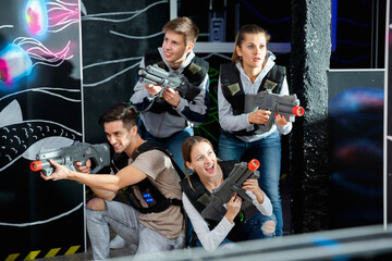 Happy young people with laser pistols posing together on dark laser tag labyrinth