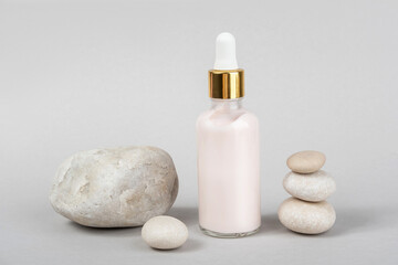 Pink anti-aging collagen, facial serum in transparent glass bottle with gold pipette and natural stones on grey background. Natural Organic Spa Cosmetic Beauty Concept. Front view
