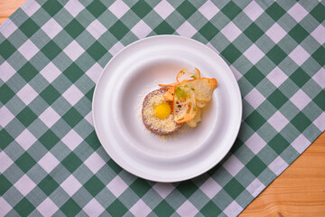 Close up of beef tartar with capers and small toasts. Served on a white plate over green plaid tablecloth background.
