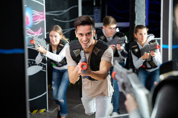Portrait of happy young man with laser pistol and playing laser tag with his friends in dark room