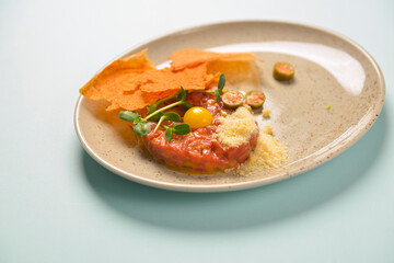 Close up of beef tartar with capers and small toasts. Served on a gray textured plate over pastel blue mint background.
